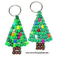 Two handmade Christmas tree keychains made with green pony beads and colorful accent beads that resemble ornaments and lights. Each hangs from a silver key ring and has a brown bead trunk.